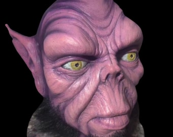May include: A detailed mask of an alien creature with a purple complexion, prominent facial features, and yellow eyes. The mask has a black beard and is set against a black background. The mask appears to be made of a durable material.