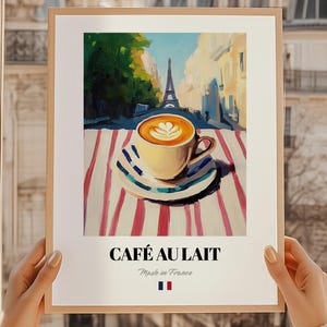 May include: A framed art print featuring a cafe scene in Paris. The artwork depicts a cup of cafe au lait on a striped tablecloth with the Eiffel Tower in the background. The text "CAFÉ AU LAIT" is displayed below the image.