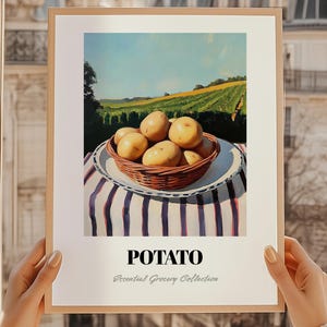 Puede incluir: Una impresión enmarcada que presenta una naturaleza muerta de patatas en una cesta de mimbre sobre un mantel a rayas. El fondo muestra un paisaje soleado con campos y un cielo azul. La palabra "POTATO" está impresa debajo.