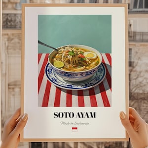 Könnte beinhalten: Gerahmter Kunstdruck mit Soto Ayam, einer traditionellen indonesischen Suppe. Die Suppe befindet sich in einer blau-weißen Schüssel auf einer rot-weiß gestreiften Oberfläche. Der Text "SOTO AYAM" steht darunter, darunter "Made in Indonesia".