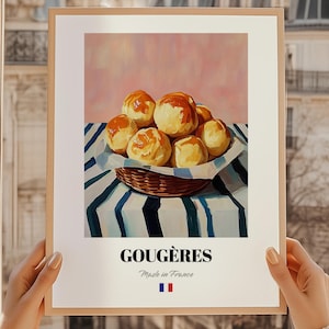 Könnte beinhalten: Ein gerahmter Druck mit Gougères, einem französischen Käsegebäck, in einem Weidenkorb auf einem gestreiften Tuch. Der Druck trägt das Wort "Gougères" und "Made in France" mit der französischen Flagge.
