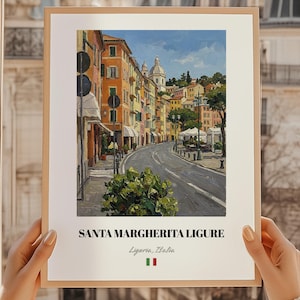 May include: A framed print of Santa Margherita Ligure, Italy. The artwork shows a vibrant street scene with buildings in orange, yellow, and pink. A road curves through the town, and the sky is blue. The print includes the text "Santa Margherita Ligure" and the Italian flag.