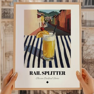 Op de afbeelding: Een ingelijste print met een cocktailillustratie. De afbeelding toont een hoog glas oranje drank, gegarneerd met een kers en een sinaasappelschijfje, op een gestreepte blauw-witte ondergrond. De tekst "RAIL SPLITTER" staat onderaan, onderdeel van de "Classic Cocktail Series".