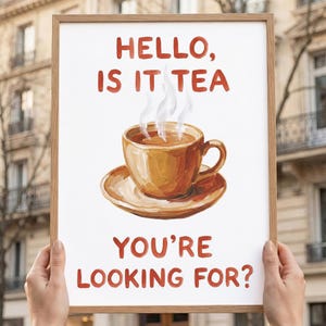 Peut inclure: Une affiche encadrée avec le texte "HELLO, IS IT TEA YOU'RE LOOKING FOR ?" au-dessus d'une illustration à l'aquarelle d'une tasse et d'une soucoupe. La tasse contient du thé et de la vapeur s'en échappe. L'affiche est tenue par deux mains.