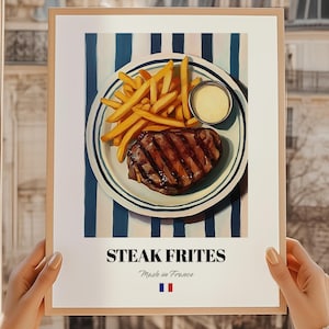 May include: A framed print featuring a plate of steak frites with a side of sauce. The steak is grilled with visible grill marks, and the fries are golden. The plate sits on a blue and white striped background. Text at the bottom reads "STEAK FRITES" and "Made in France".