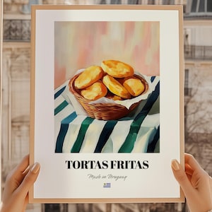 May include: A framed print depicting a still life of golden-brown fried pastries in a woven basket, set against a striped tablecloth. The print includes the text "TORTAS FRITAS" and "Made in Uruguay" with a small flag.