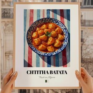 以下が含まれることがあります： 伝統的なアルジェリアのジャガイモ料理、Chtitha Batataの鮮やかなイラストが描かれた額入りのプリント。 青と白の模様のボウルに入った料理は、赤、白、青のストライプの背景に配置されています。 テキスト「CHTITHA BATATA」と「Made in Algeria」が表示されています。