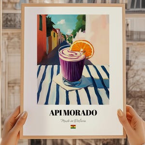 May include: A framed art print featuring a vibrant illustration of a purple drink with a whipped topping and an orange slice. The artwork is set against a backdrop of a street scene with colorful buildings. The text "API MORADO" is displayed at the bottom.