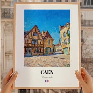 Può includere: Una stampa incorniciata con un dipinto di Caen, Francia. L'opera raffigura edifici colorati e una strada acciottolata sotto un cielo blu brillante. La stampa include il nome della città e la bandiera francese.