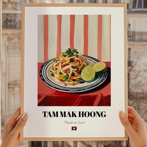 Peut inclure: Une affiche encadrée représentant une illustration colorée de Tam Mak Hoong, avec des tranches de citron vert sur une assiette. Le fond est orné de rayures rouges et blanches. Le texte "TAM MAK HOONG" est affiché en bas, avec "Made in Laos" en dessous.