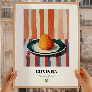 Puede incluir: Una impresión enmarcada que presenta un Coxinha, un popular aperitivo brasileño, en un plato. La obra de arte tiene un fondo a rayas en rojo, blanco y naranja. El texto "COXINHA" se muestra debajo de la imagen, con "Made in Brazil" y una bandera brasileña.