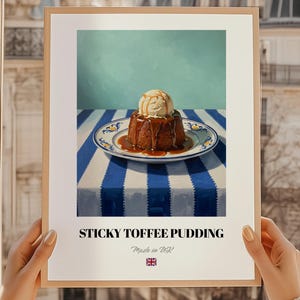 May include: A framed print featuring a still life of sticky toffee pudding with ice cream and caramel sauce on a blue and white striped tablecloth. The text "STICKY TOFFEE PUDDING" is displayed below the image, with "Made in UK" and a UK flag.