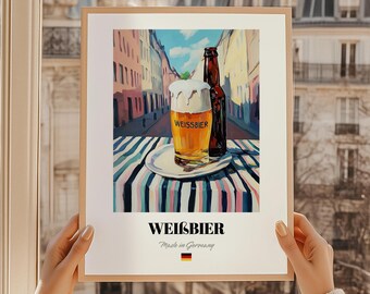 May include: A framed print featuring a glass of Weissbier with a foamy head, a brown bottle, and a striped tablecloth. The background depicts a European street scene. The text "WEISSBIER" is displayed above "Made in Germany" with a German flag.