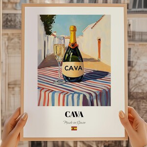 May include: A framed print featuring a bottle of Cava sparkling wine and a filled glass on a striped tablecloth. The bottle is green with a gold foil top and a label that reads "CAVA". The print includes the text "CAVA Made in Spain".