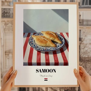 May include: A framed print featuring two samoons on a decorative plate with a blue and white design, set against a red and white striped tablecloth. The print includes the text "SAMOON Made in Iraq".