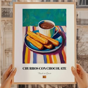 May include: A framed print featuring a vibrant illustration of churros and chocolate. The image shows a white cup of hot chocolate, churros on a blue plate, and the text "CHURROS CON CHOCOLATE" with "Made in Spain" below it.