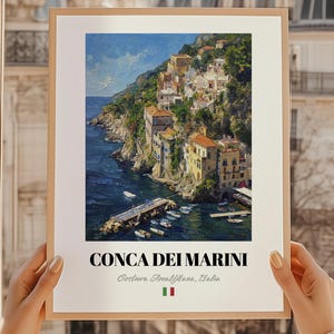 Puede incluir: Una impresión enmarcada de Conca dei Marini, Italia, que muestra un pueblo costero con edificios coloridos en un acantilado. La obra de arte representa un vibrante paisaje marino con botes y un muelle, con el texto "CONCA DEI MARINI" en la parte inferior.