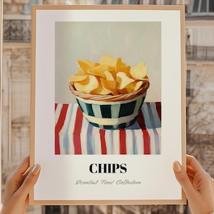 Könnte beinhalten: Ein gerahmter Druck mit einem Stillleben von Kartoffelchips in einer gestreiften Schüssel. Die Schüssel steht auf einer rot-weiß-blau gestreiften Tischdecke. Das Wort "CHIPS" ist unter dem Bild aufgedruckt, darunter "Essential Food Collection".