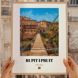Peut inclure: Une impression encadrée présentant une peinture impressionniste d'un pont et de bâtiments. L'œuvre d'art montre un ciel bleu et un pont en bois. Le texte "RUPIT I PRUIT" est en bas, avec "Cataluña" et un drapeau espagnol.