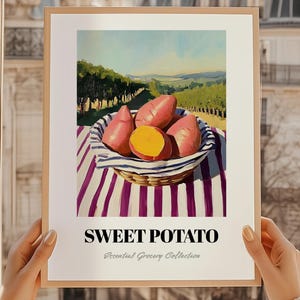 Könnte beinhalten: Ein gerahmter Kunstdruck mit Süßkartoffeln in einem Weidenkorb. Der Korb steht auf einem gestreiften Tuch, im Hintergrund ein Weinberg und Hügel. Der Text "SWEET POTATO" ist unter dem Bild zu sehen. Teil der Essential Grocery Collection.