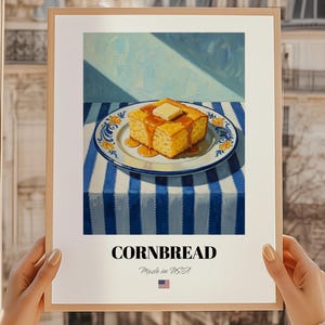 Peut inclure: Une affiche encadrée représentant du pain de maïs avec du beurre et du sirop sur une assiette décorative. L'assiette est posée sur une nappe à rayures bleues et blanches. Le mot "CORNBREAD" est imprimé en gras, avec "Made in USA" en dessous.