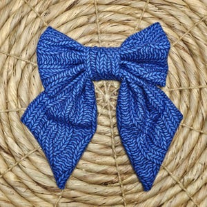May include: A blue bow tie with a textured knit pattern. The bow tie is a vibrant shade of blue with a darker blue pattern. The bow tie is made of fabric and is set against a woven background.