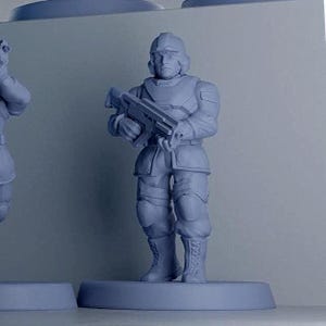 Op de afbeelding: Een lichtgrijs, onbeschilderd miniatuurfiguur van een soldaat die op een ronde voet staat. Het figuur draagt een helm, tactisch vest en laarzen, en houdt een geweer met beide handen vast. Het oppervlak van het kunststof model is glad en mat.