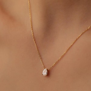 May include: A delicate gold chain necklace with a pear-shaped clear gemstone pendant.