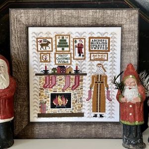 May include: A framed cross-stitch depicting a festive Christmas scene with a fireplace, stockings, and Santa Claus figures. The text "Merry Christmas Wishes" and "And to all a Goodnight" are visible. Two Santa Claus figurines are in the foreground.