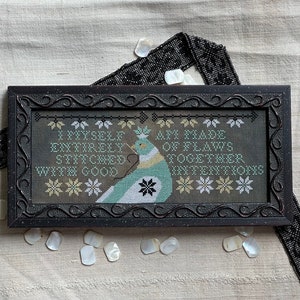May include: A framed cross-stitch design featuring a stylised bird with the text "I myself am made entirely of flaws stitched together with good intentions".