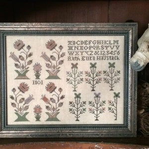 Könnte beinhalten: Ein gerahmter Kreuzstich-Sampler mit einem floralen Design und dem Text "A B C D E F G H I J K L M N O P Q R S T U V W X Y Z & 1 2 3 4 5 6 Ruth Even Maystack 1801".