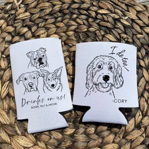 Op de afbeelding: Twee witte blikjeskoelers met zwarte lijntekeningen van honden. E&eacute;n koeler heeft drie hondenportretten en de tekst "Drinks on us!" en "Boxer, Tilly & Archie". De andere heeft een hondenportret en de tekst "I do too." en "-Cory".
