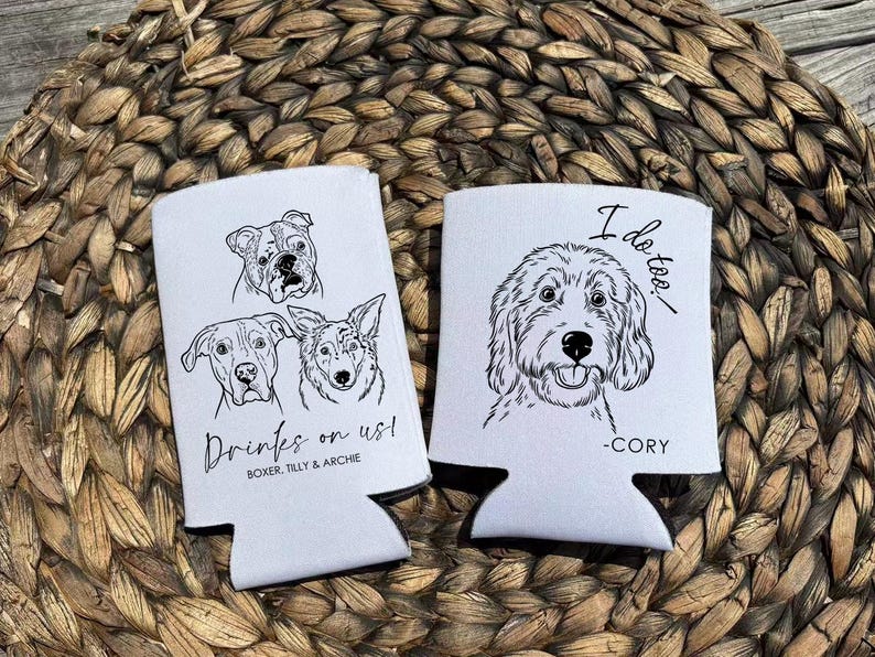 Op de afbeelding: Twee witte blikjeskoelers met zwarte lijntekeningen van honden. E&eacute;n koeler heeft drie hondenportretten en de tekst "Drinks on us!" en "Boxer, Tilly & Archie". De andere heeft een hondenportret en de tekst "I do too." en "-Cory".
