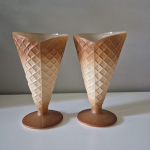 Puede incluir: Dos vasos con forma de cono de helado. Los vasos son marrones y beiges con un patrón de diamantes. La base es de color marrón liso. Los vasos están sobre una superficie blanca.