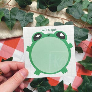 Könnte beinhalten: Ein grüner, froschförmiger Haftzettel mit dem Text "don't froget:" oben. Der Frosch hat große schwarze Augen und kleine Arme und Beine. Der Hintergrund ist ein Rastermuster.