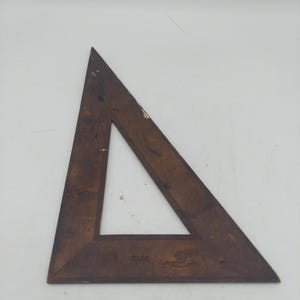 May include: A dark brown wooden triangle drafting tool with a right-angle shape. The surface shows signs of wear, including small scratches, scuffs, and minor paint marks. The wood grain is visible throughout the frame of the geometric instrument.