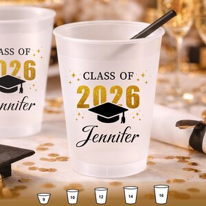 May include: A frosted plastic party cup featuring the black text "CLASS OF" above the gold glitter numbers "2026" and a black graduation cap icon. The name "Jennifer" is printed in black script below. A black straw is inside the cup.