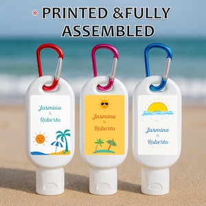 May include: Three white hand sanitizer bottles with colorful carabiner clips. Each bottle has a label with a beach-themed design and the names "Jasmina & Roberto." The text "PRINTED & FULLY ASSEMBLED" is at the top.
