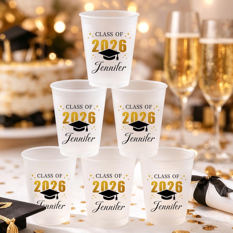 May include: A set of six frosted plastic cups featuring the text "CLASS OF 2026" in gold glitter, a black graduation cap icon, and the name "Jennifer" in black script. The cups are arranged in a pyramid stack for a graduation celebration.