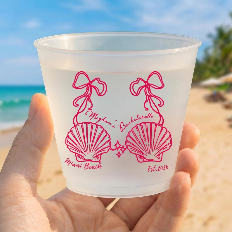 May include: A translucent frosted plastic cup featuring a hot pink graphic of two seashells connected by ribbons. The text reads "Meghan's Bachelorette" in the center, "Miami Beach" on the bottom left, and "Est. 2026" on the bottom right.