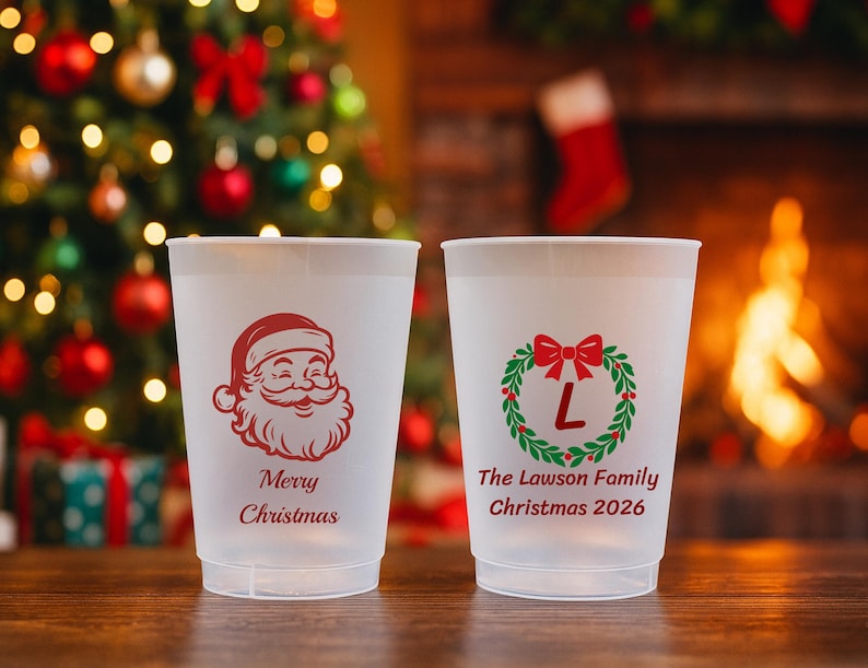 May include: Two frosted plastic cups. The left cup features a red Santa Claus graphic with the text Merry Christmas. The right cup displays a green and red wreath with a red letter L in the center and the text The Lawson Family Christmas 2026.