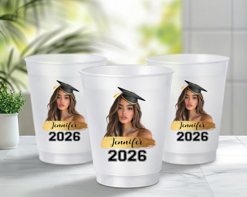 May include: Three translucent white plastic cups featuring a printed graphic of a person wearing a black graduation cap. Below the image is a gold brushstroke design with the name Jennifer in black script and the year 2026 in bold black font.