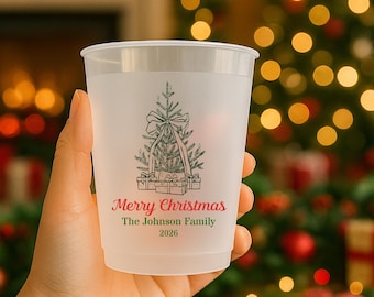 May include: A frosted plastic cup featuring a green line-art illustration of a Christmas tree with a bow and wrapped gifts at the base. Below the tree, the text reads Merry Christmas in red, followed by The Johnson Family and 2026 in green.