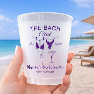 Może przedstawiać: P&oacute;łprzezroczysty plastikowy kubek z fioletowym tekstem i grafikami. Projekt zawiera napisy THE BACH CLUB, Est 2026, Martin's Bachelorette oraz NEW YORK, NY, a także ilustracje bikini, fig od stroju kąpielowego oraz kieliszka do martini.