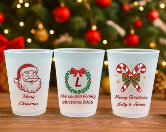May include: Three frosted plastic cups featuring Christmas designs. The first shows a red Santa face with "Merry Christmas". The second has a green wreath with a red bow, "L", "The Lawson Family", and "Christmas 2026". The third has candy canes, "Merry Christmas", and "Ketty & James".