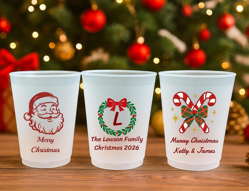 May include: Three frosted plastic cups featuring Christmas designs. The first shows a red Santa face with "Merry Christmas". The second has a green wreath with a red bow, "L", "The Lawson Family", and "Christmas 2026". The third has candy canes, "Merry Christmas", and "Ketty & James".