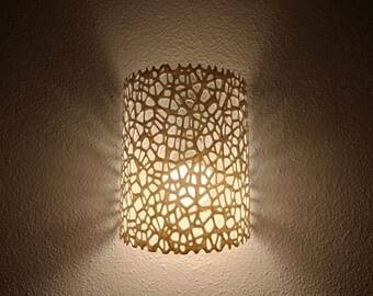 May include: A white, decorative wall sconce with a light bulb inside. The sconce has a geometric, web-like design.
