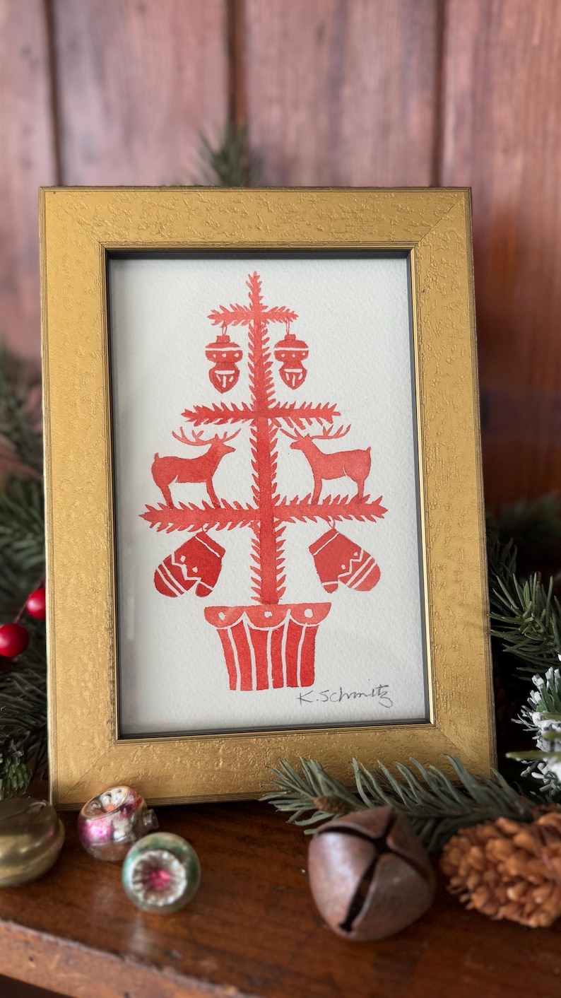 K&ouml;nnte beinhalten: Ein gerahmter Druck in einem goldfarbenen Rahmen. Der Druck zeigt ein rotes Weihnachtsbaumdesign mit Hirschen, Ornamenten und F&auml;ustlingen. Die Signatur des K&uuml;nstlers, "K.Schmitz", ist unten rechts sichtbar.