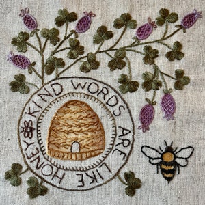 May include: Embroidered design on a beige fabric with a bee, a honeycomb, and the text "Kind words are like honey".