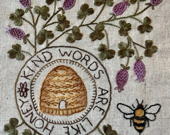 May include: Embroidered design on a beige fabric with a bee, a honeycomb, and the text "Kind words are like honey".